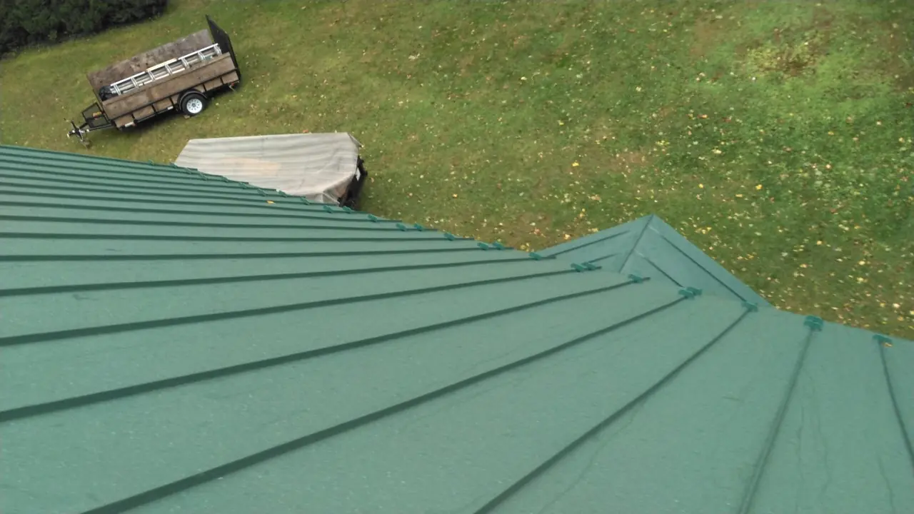 Green standing seam hip and panel lines with a trailer in the yard.