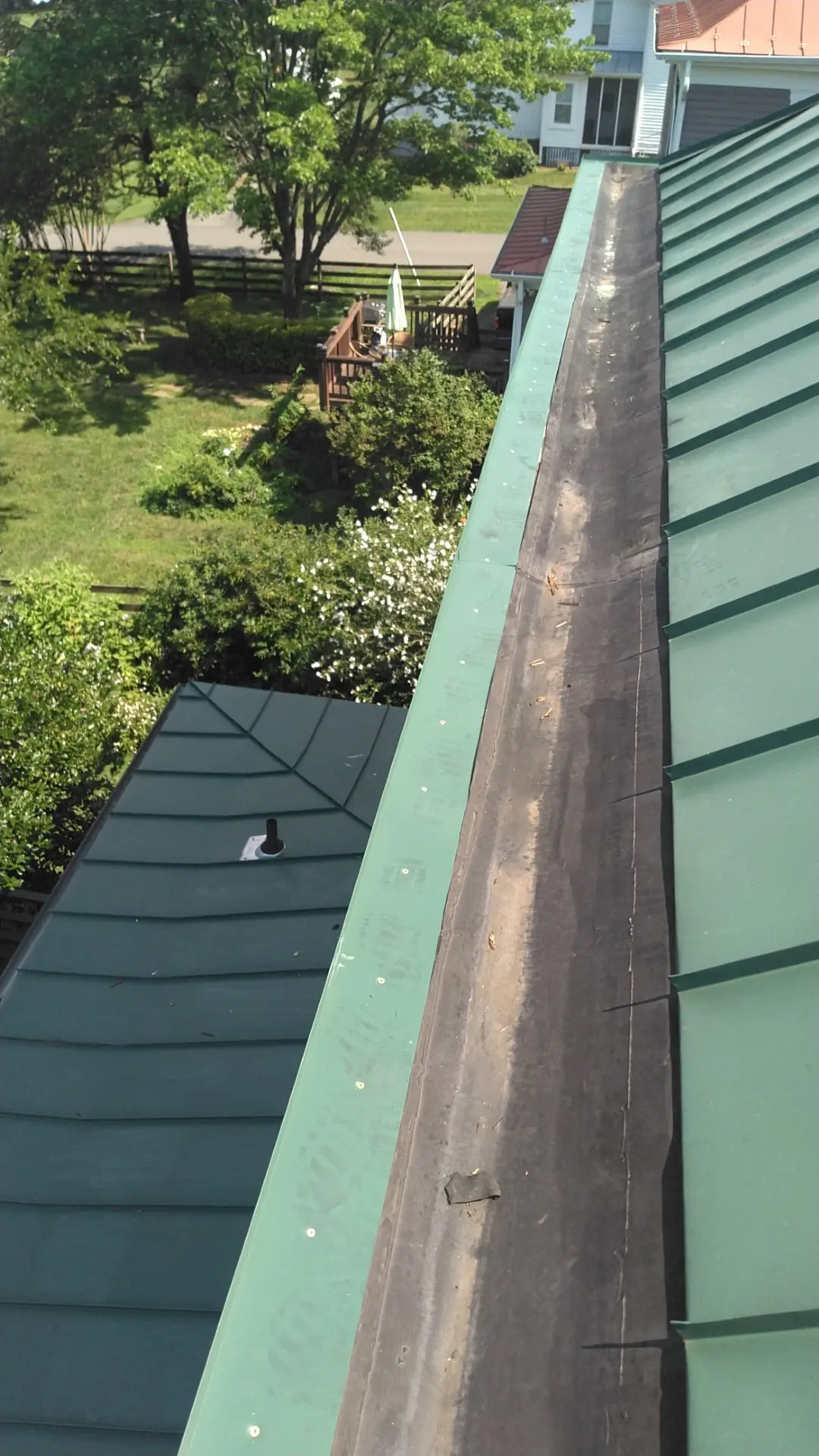 Long built-in gutter running beside a green metal roof over a lawn.