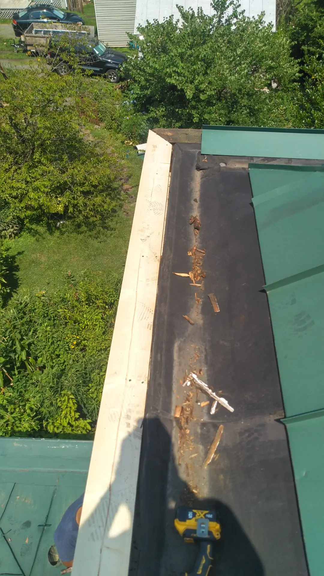 Built-in gutter meeting the green metal roof at a corner above a grassy yard.