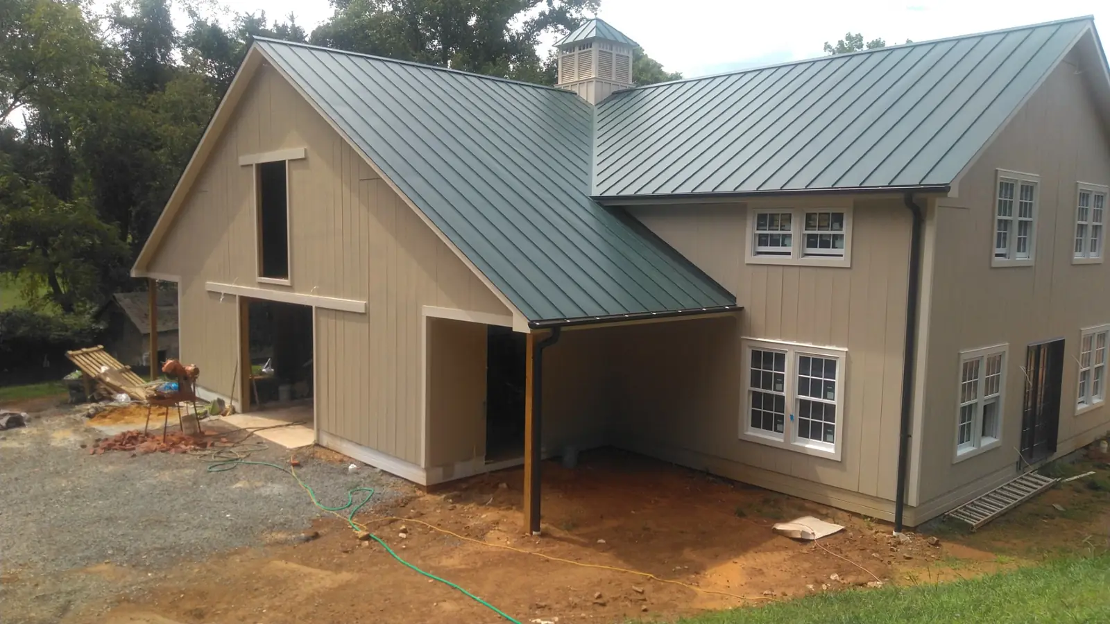 Home with a green metal roof, open barn-style doors and a dirt lot being graded.