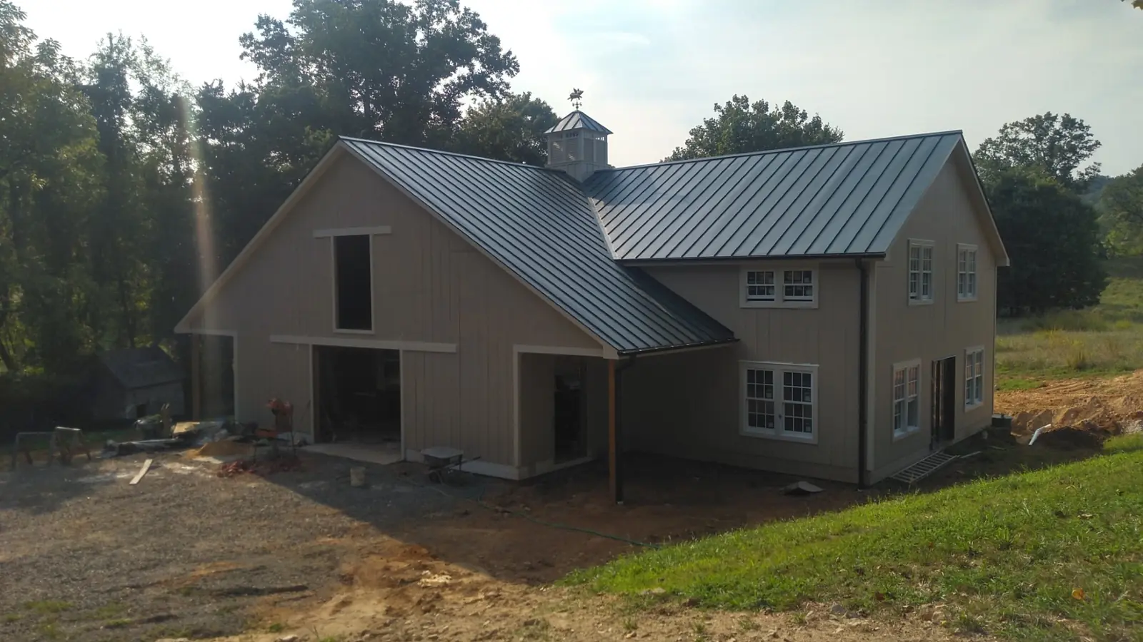 Barn-style home with a green metal roof seen across a freshly seeded lawn.