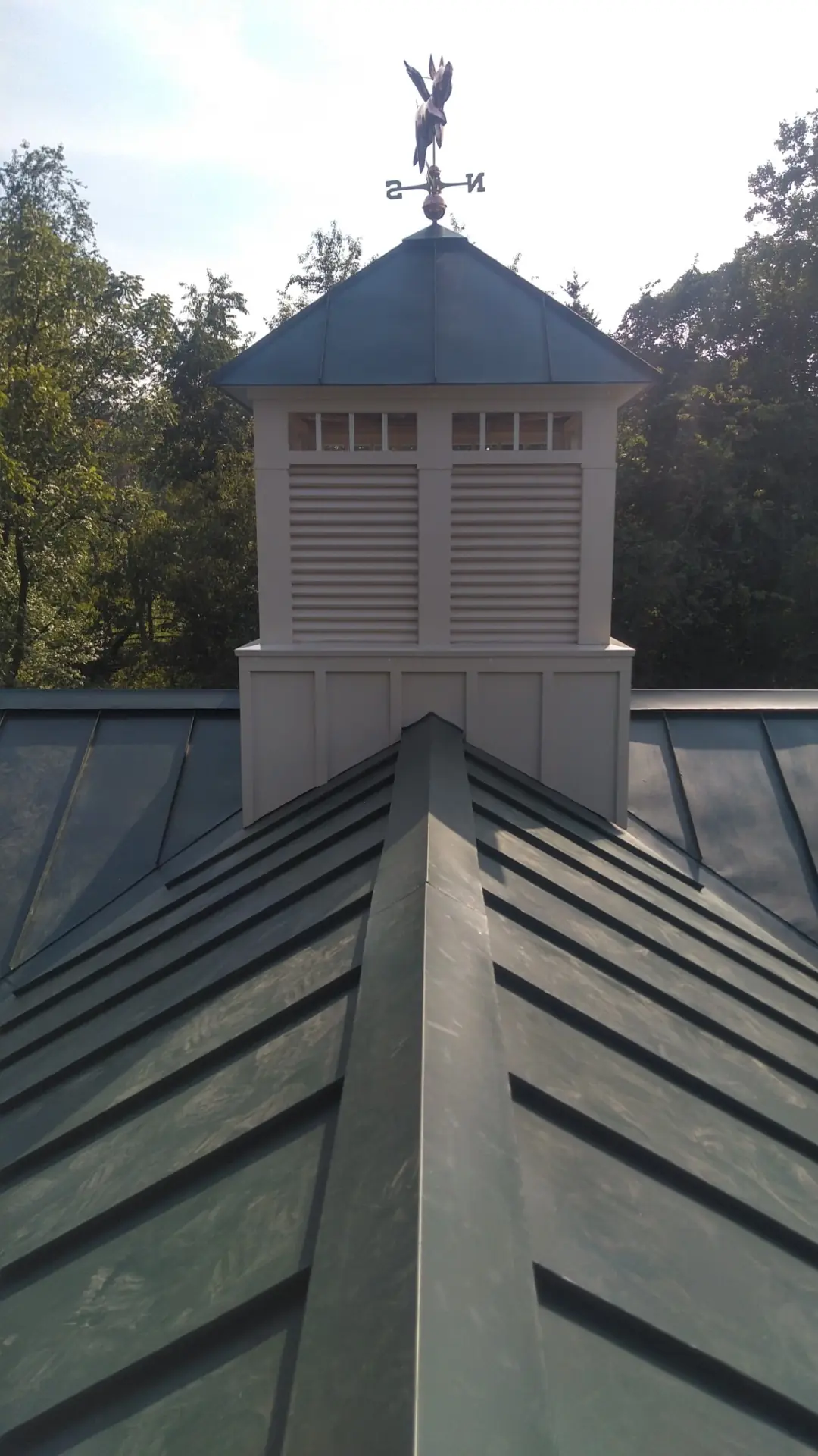 White cupola with a weather vane on a green standing seam roof.