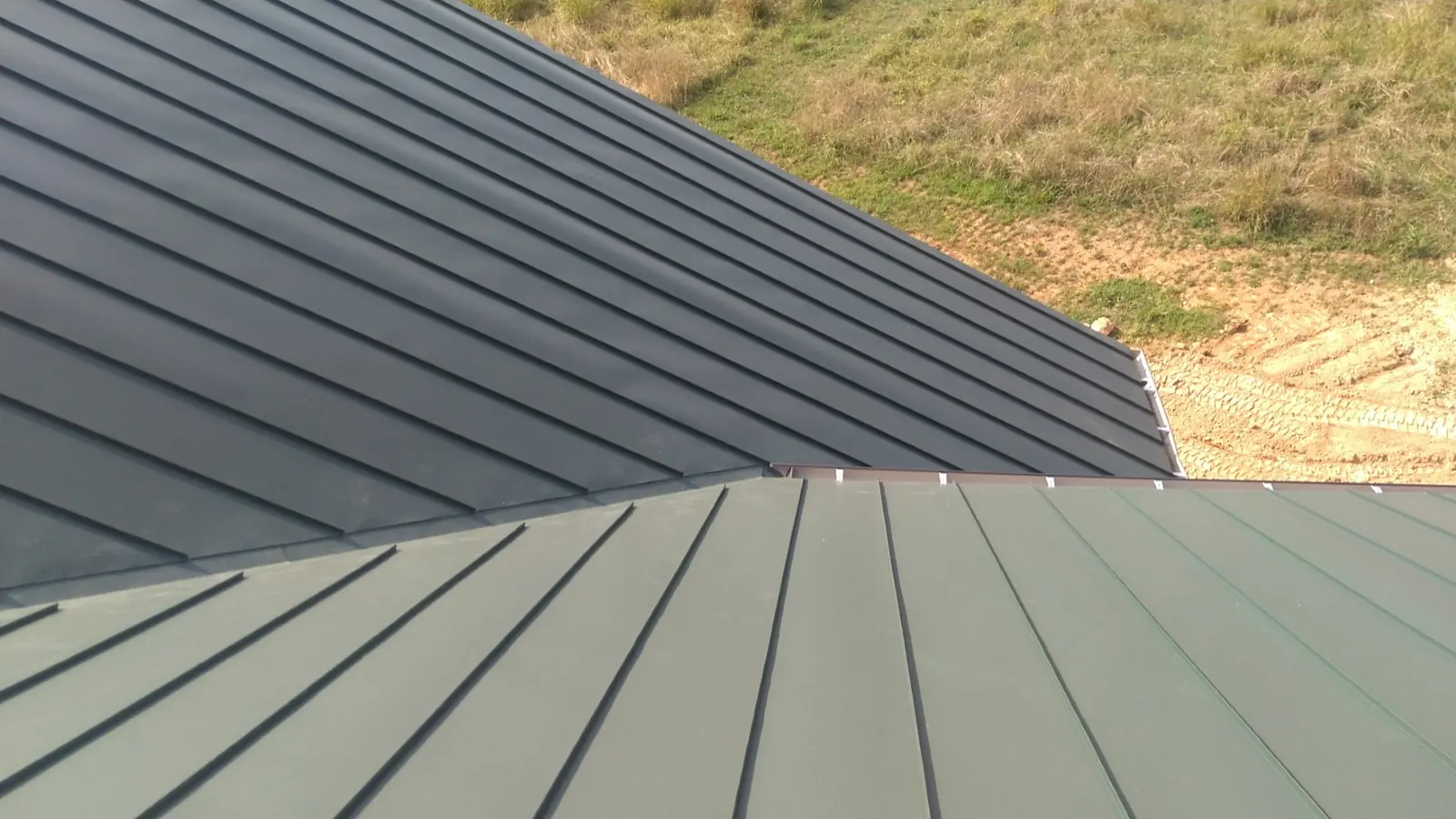 Dark green standing seam roof and rake edge above a hillside.