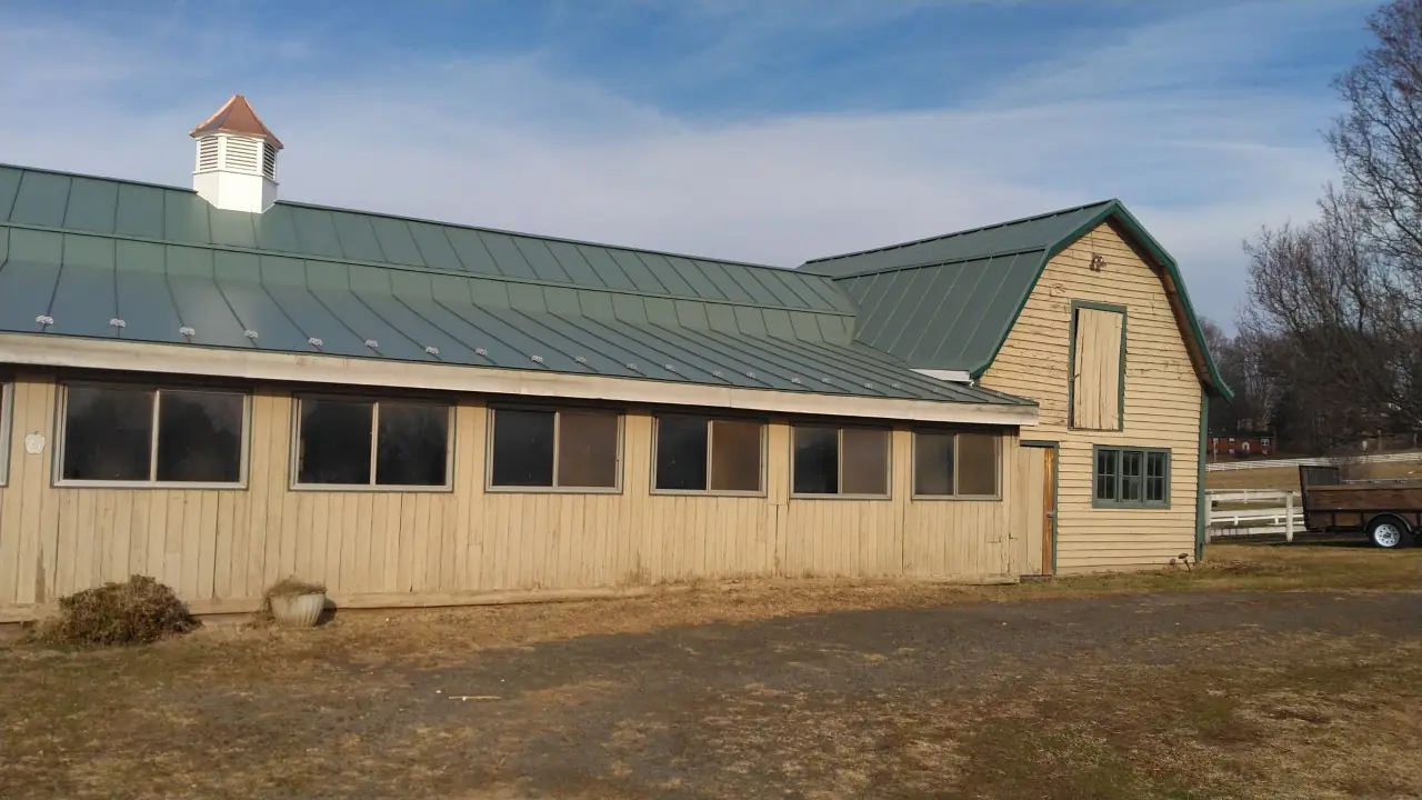 Long stable building with a Hemlock green standing seam roof and a cupola.