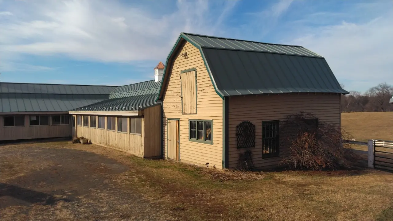 Gambrel barn with a green metal roof beside a long stable building.