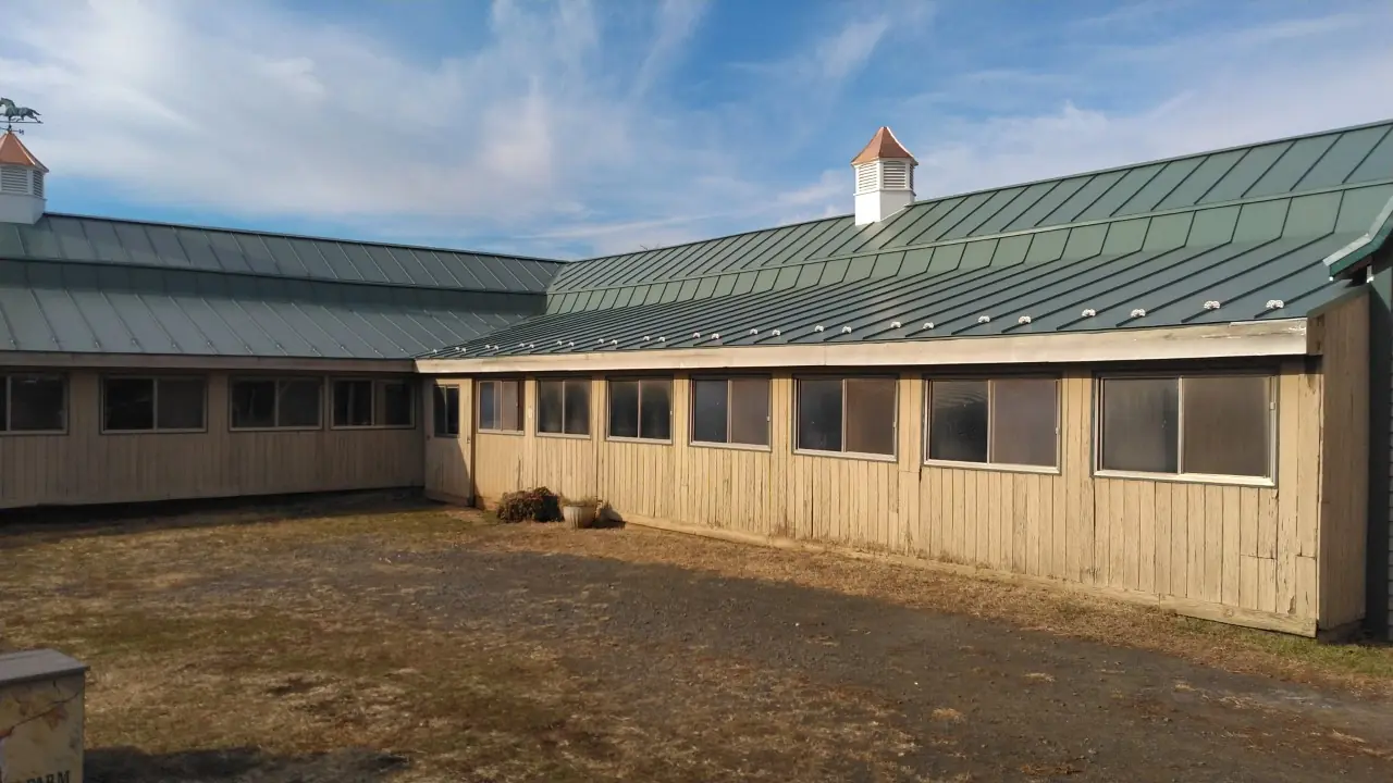 Long stable with tall windows and a green metal roof around a gravel courtyard.