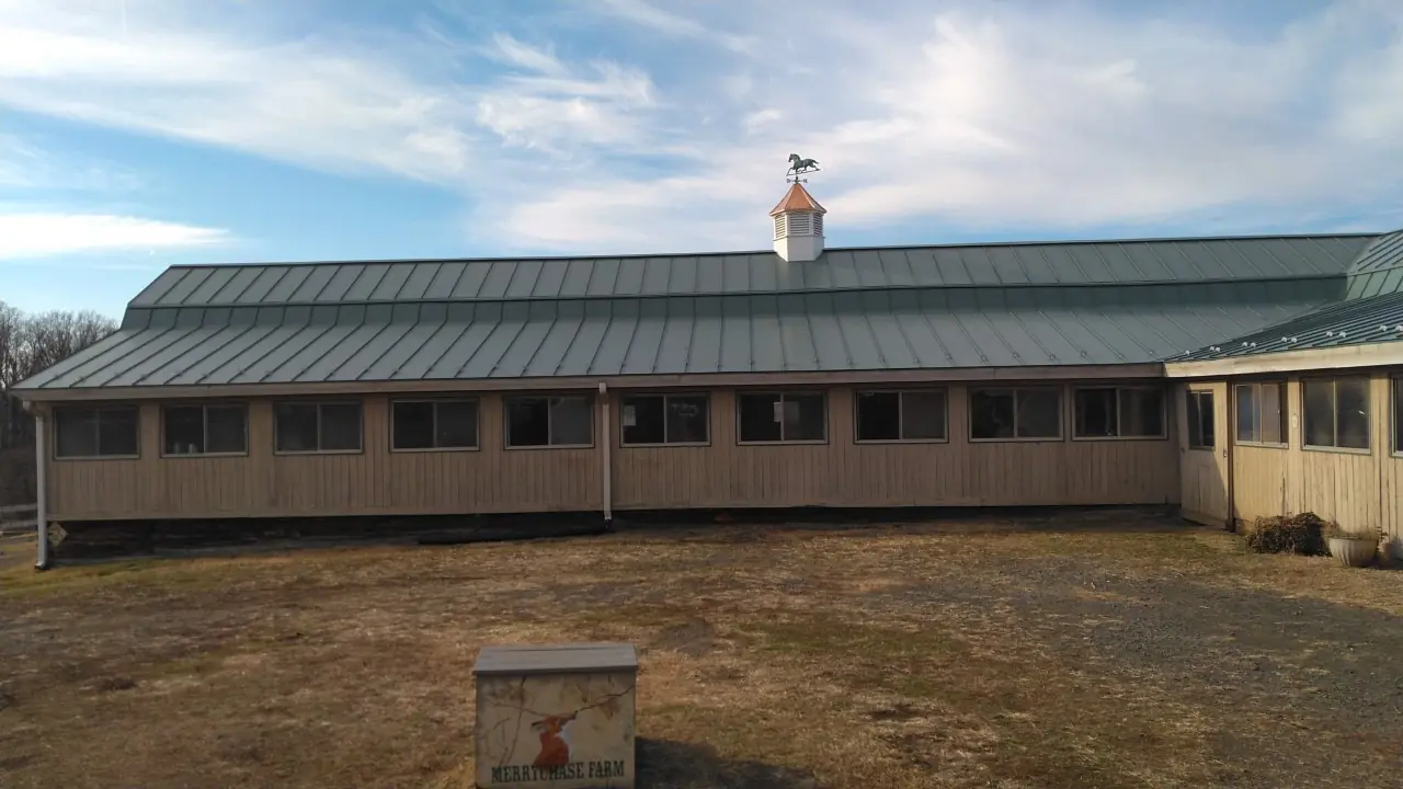Stable and a green metal roof under a blue sky.