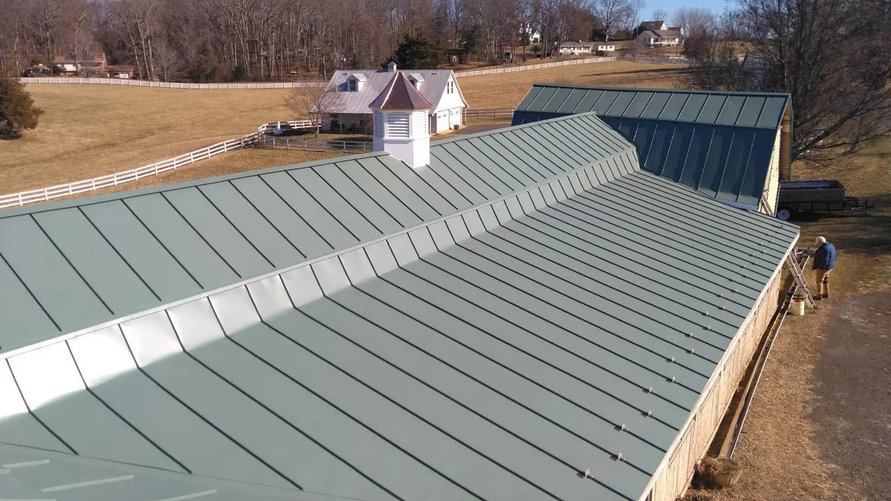 Green standing seam stable roof with a cupola and white fencing beyond.