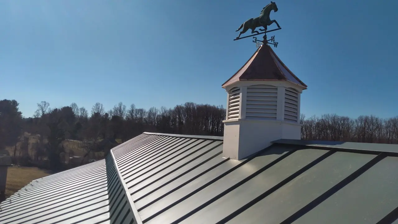Cupola with a horse weather vane over a green standing seam ridge.