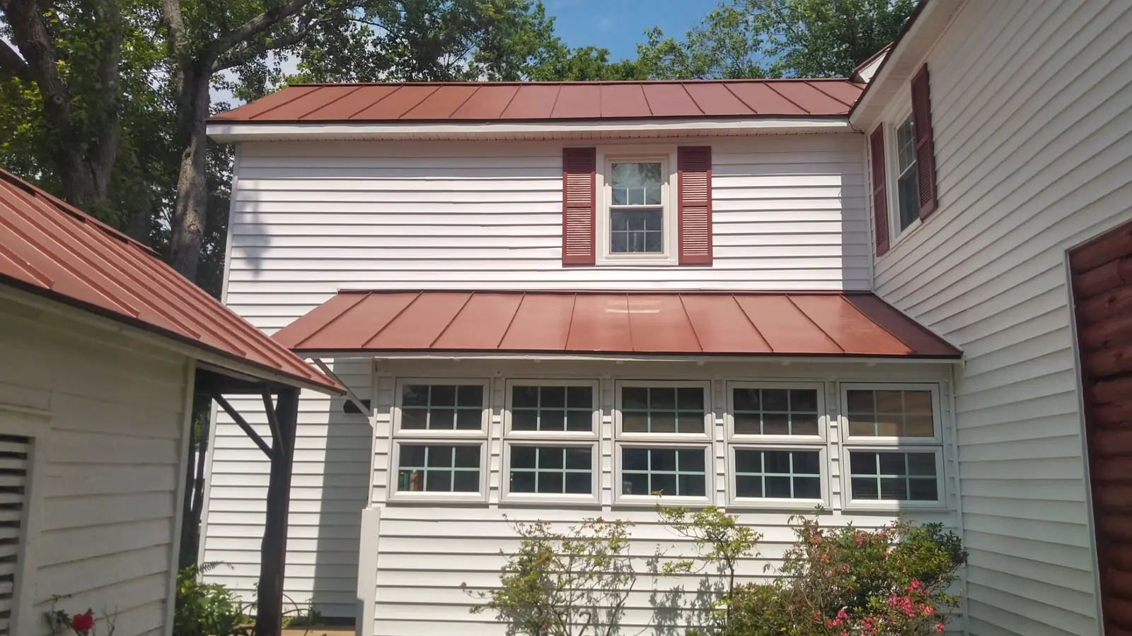Red standing seam roof over the porch and a bank of windows on a white-sided house.