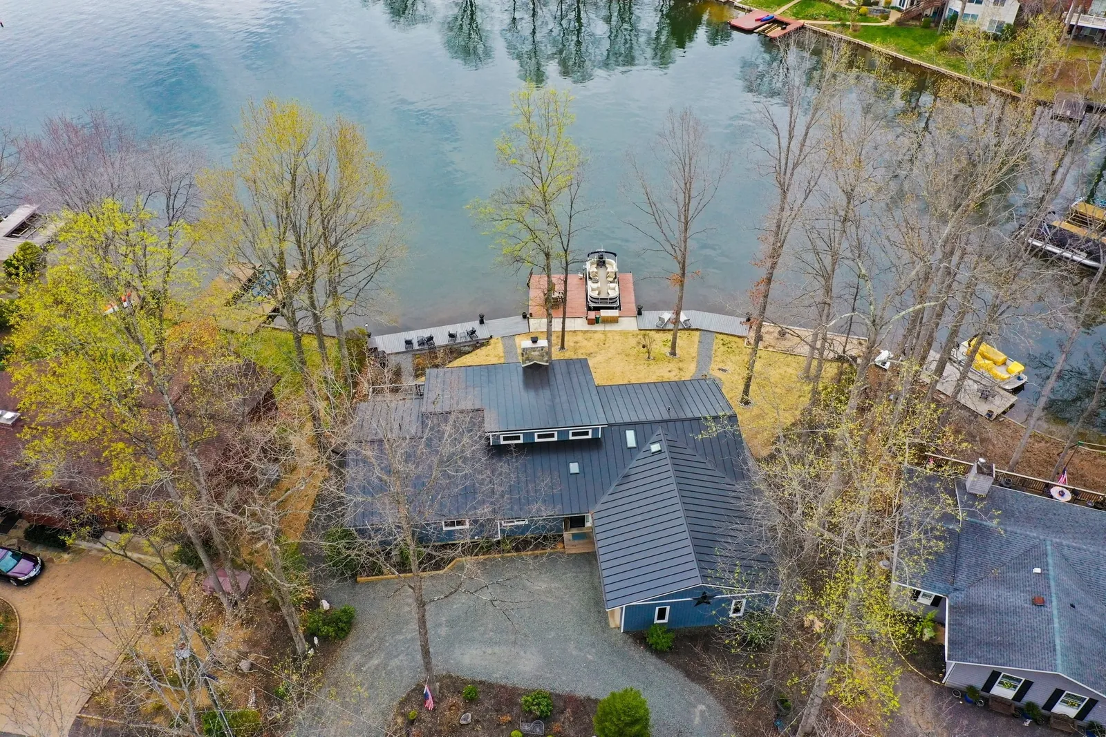 Aerial view of a lakeside home with a dark roof, dock and wooded shoreline.