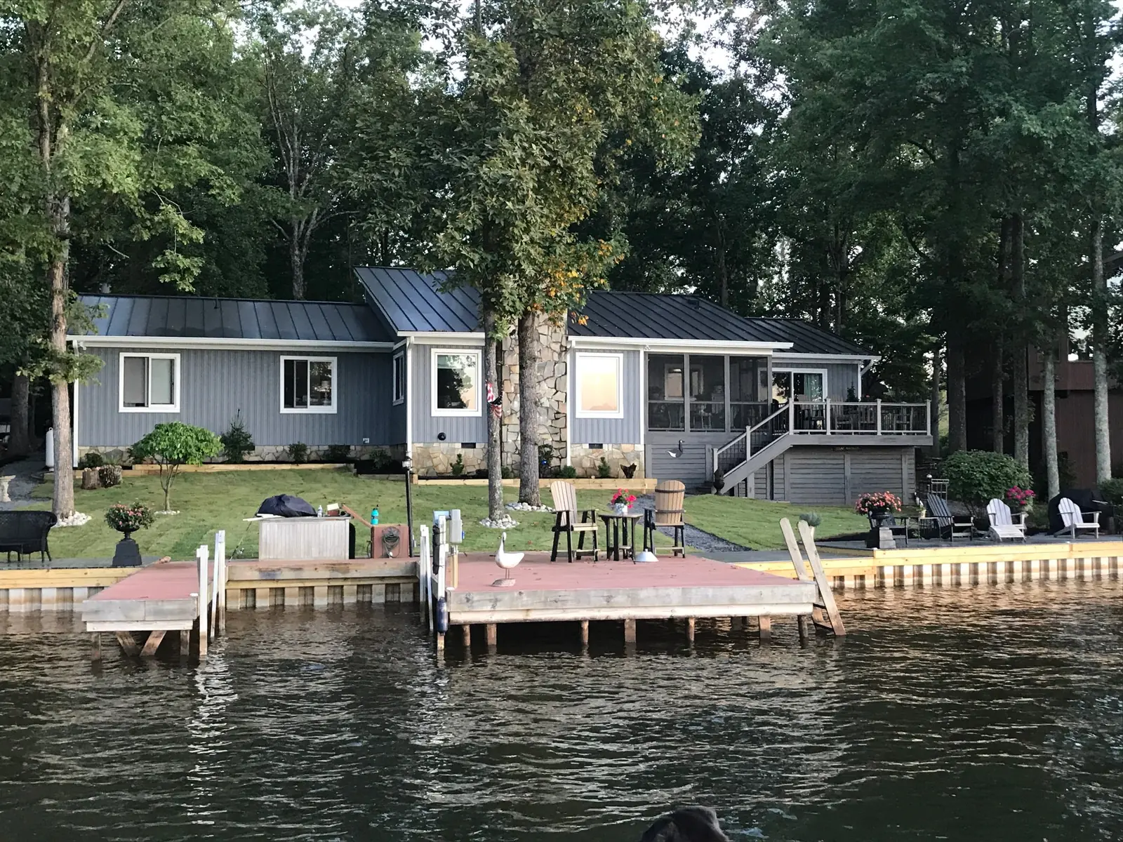 Blue-gray lakeside home with a dark metal roof and a dock on calm water.