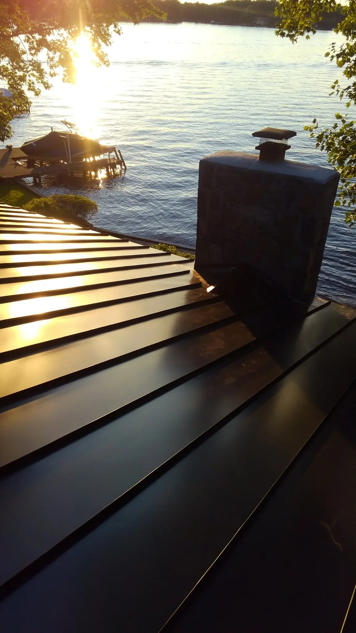 Dark metal roof with a brick chimney and the lake behind at sunset.