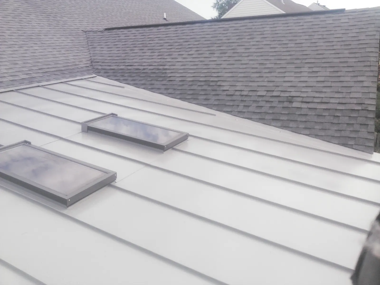Light gray standing seam roof with skylights beside gray shingles.