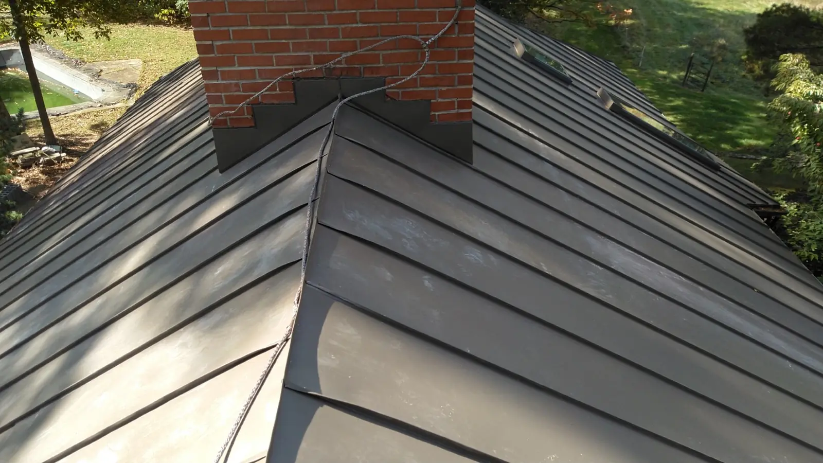 Bronze standing seam hip beside a brick chimney.