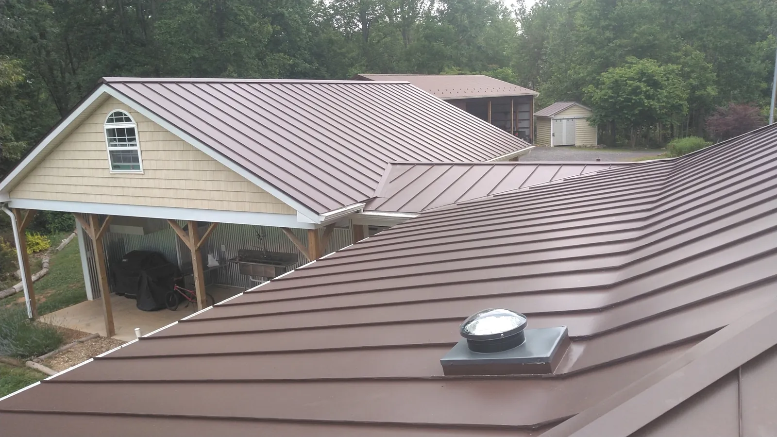 Brown standing seam metal roof running over a hip roof and covered porch with a roof-mounted skylight.