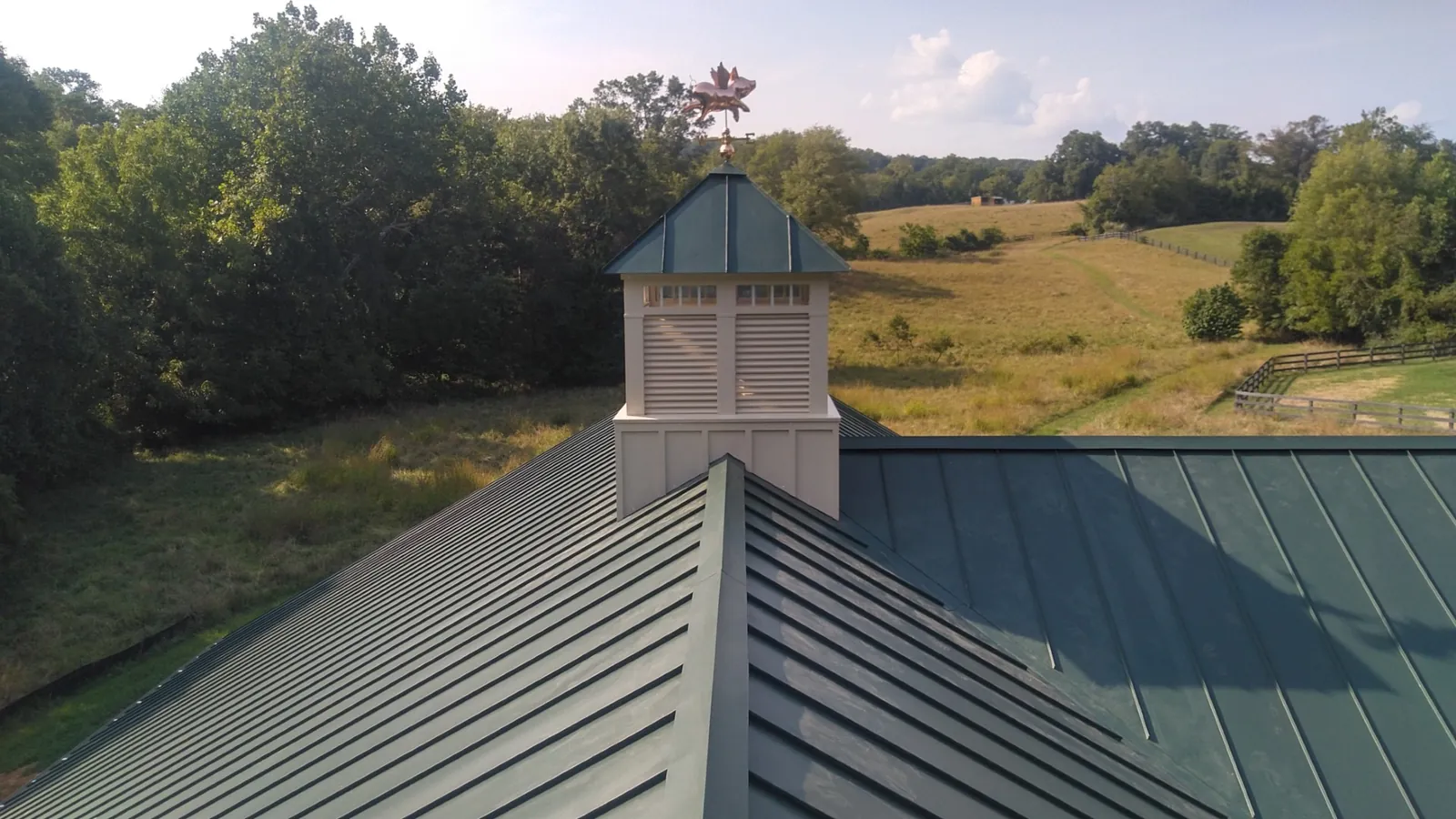 Green standing seam metal roof with a cupola overlooking open farmland.