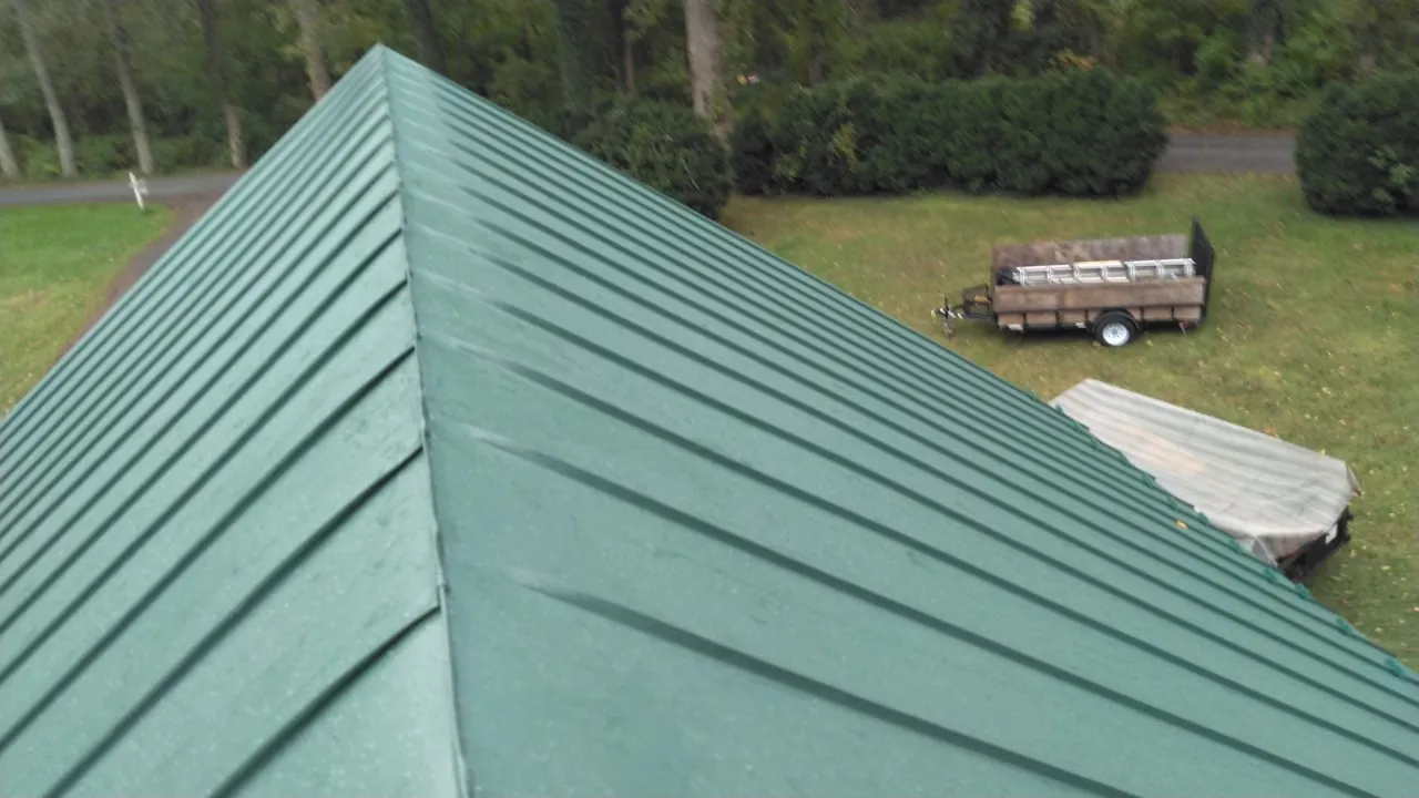Green standing seam roof ridge and panel lines against a rural lawn.