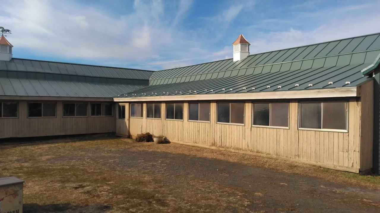 Long outbuilding with a green metal roof and a cupola across a gravel courtyard.