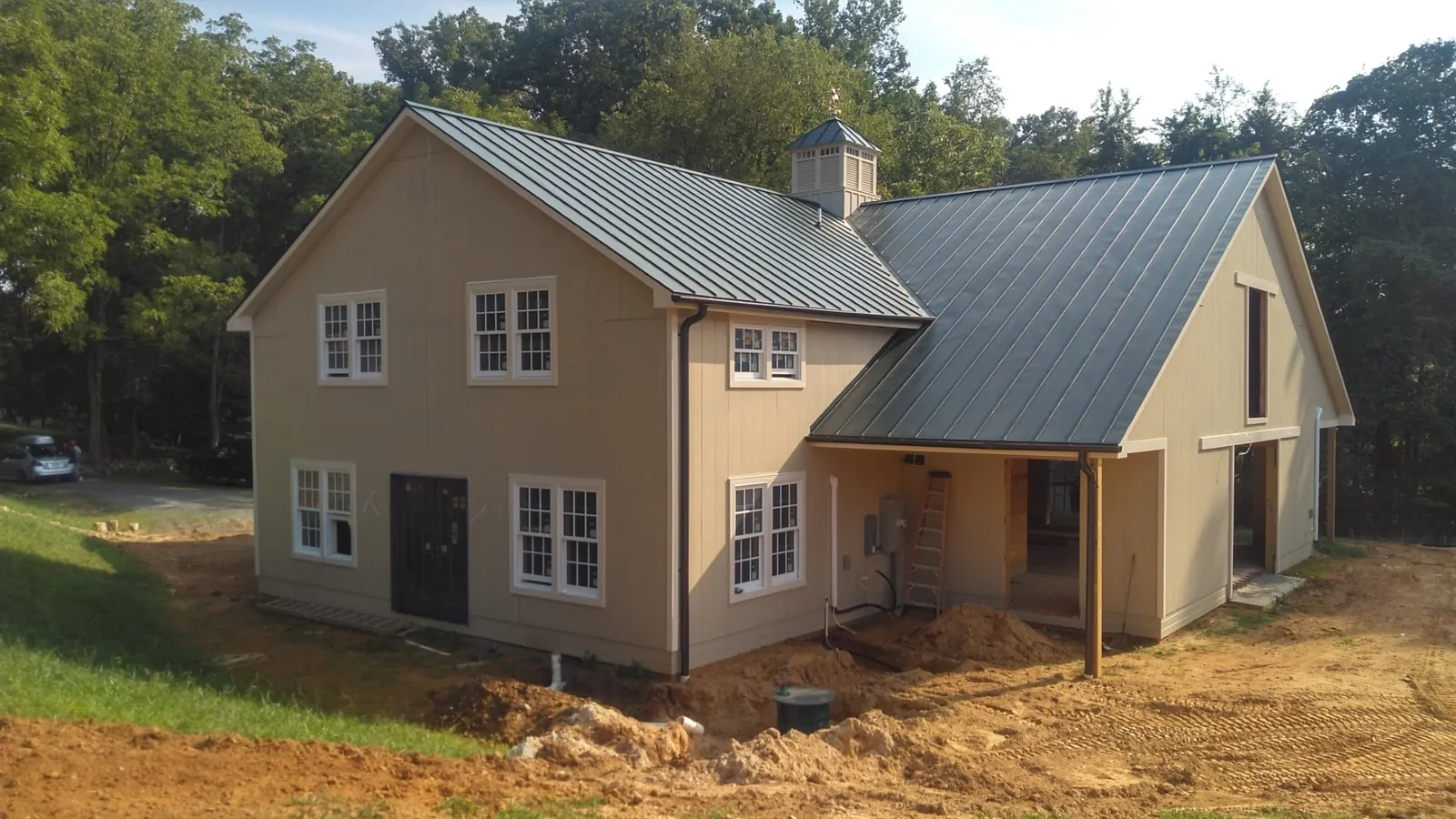Newly built home with a dark standing seam metal roof and tan siding before landscaping.