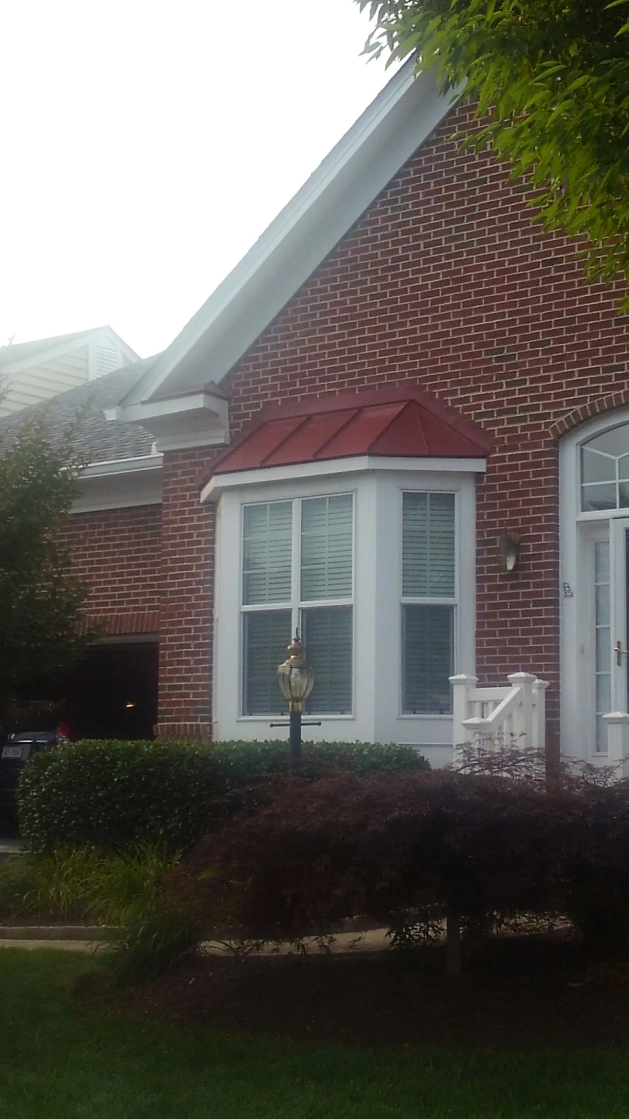 Brick home with a red metal roof over a bay window and a lawn in front.