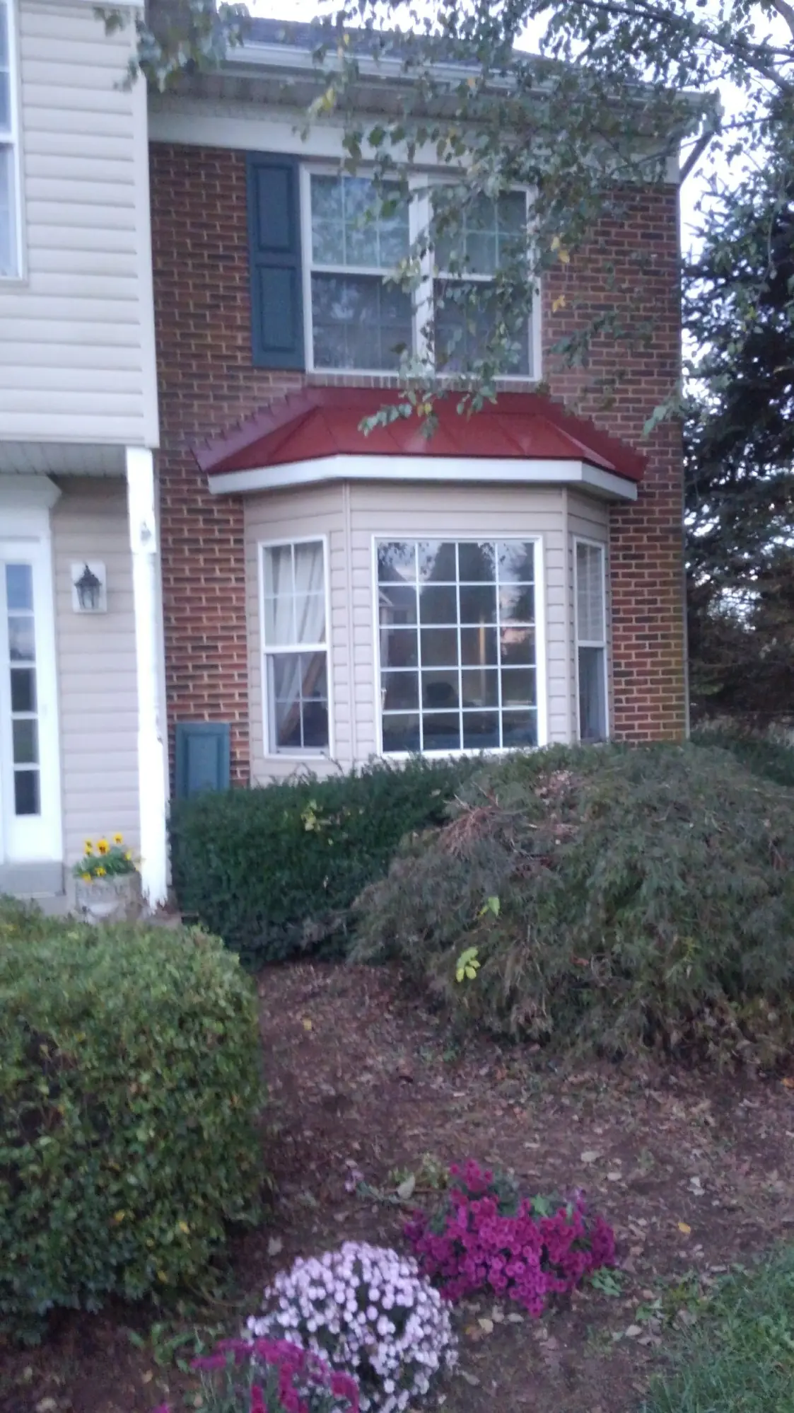 White-trimmed bay window under a red metal roof on a brick home.