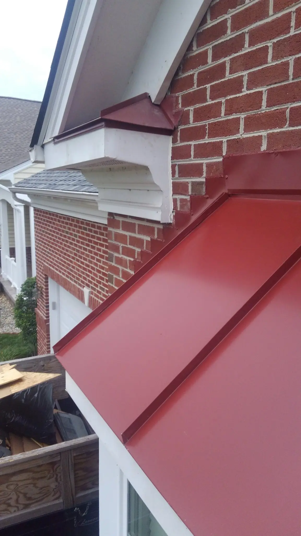Red standing seam panel at the corner of a brick wall.