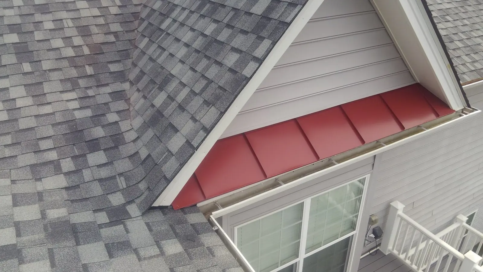 Red metal accent under a gable window on a home with gray shingles.