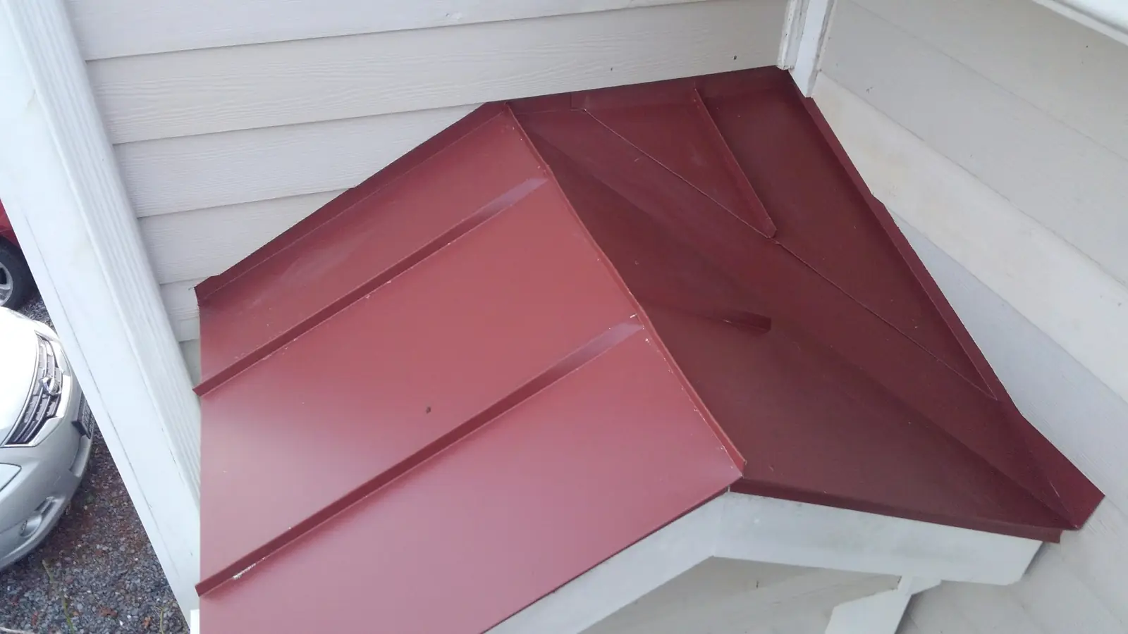 Red metal hood over a corner entry on a white-trimmed house.