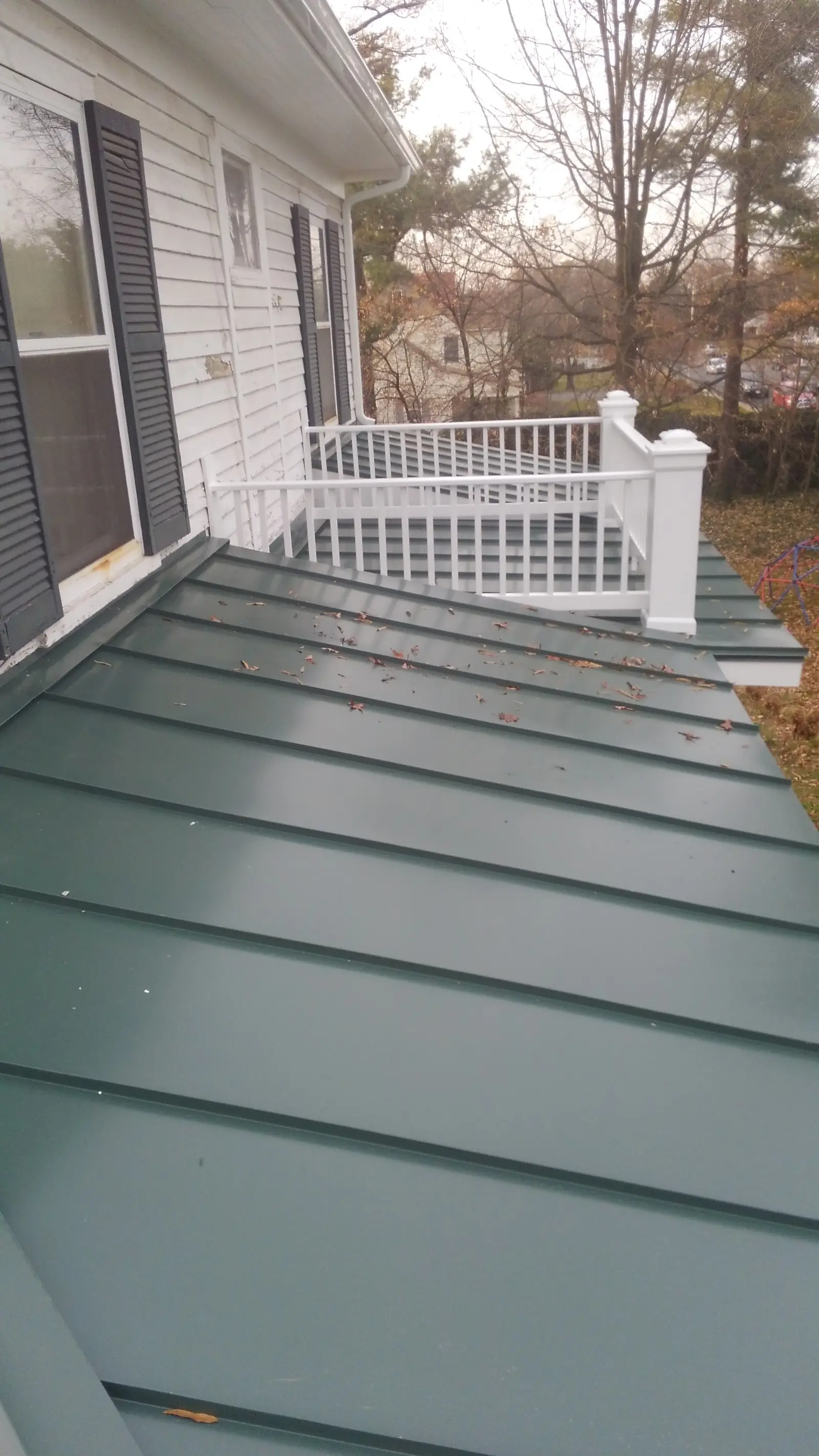 Green standing seam porch roof running along a white railing.