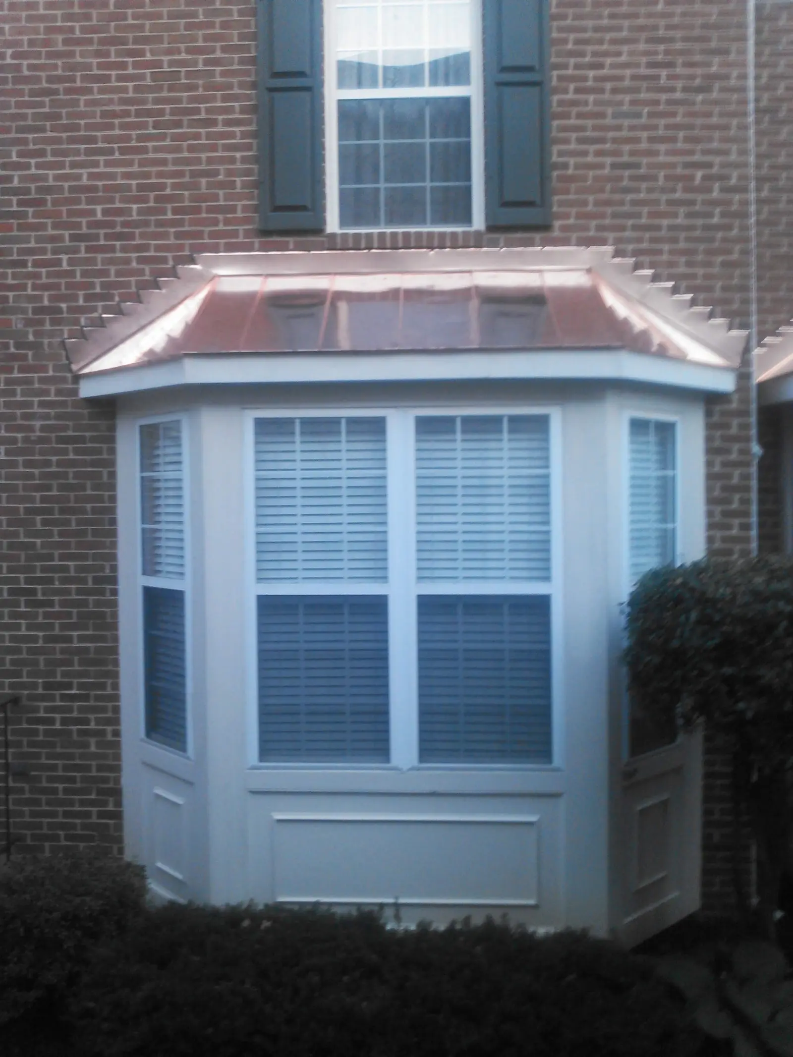Copper roof over a white bay window on a brick wall.