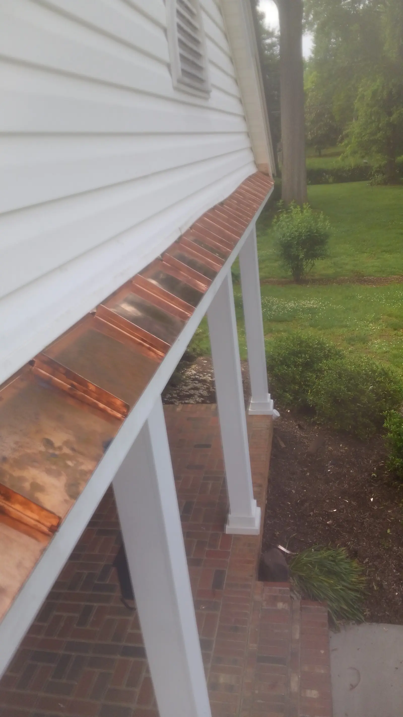 Copper gutter along a porch eave beside white columns.