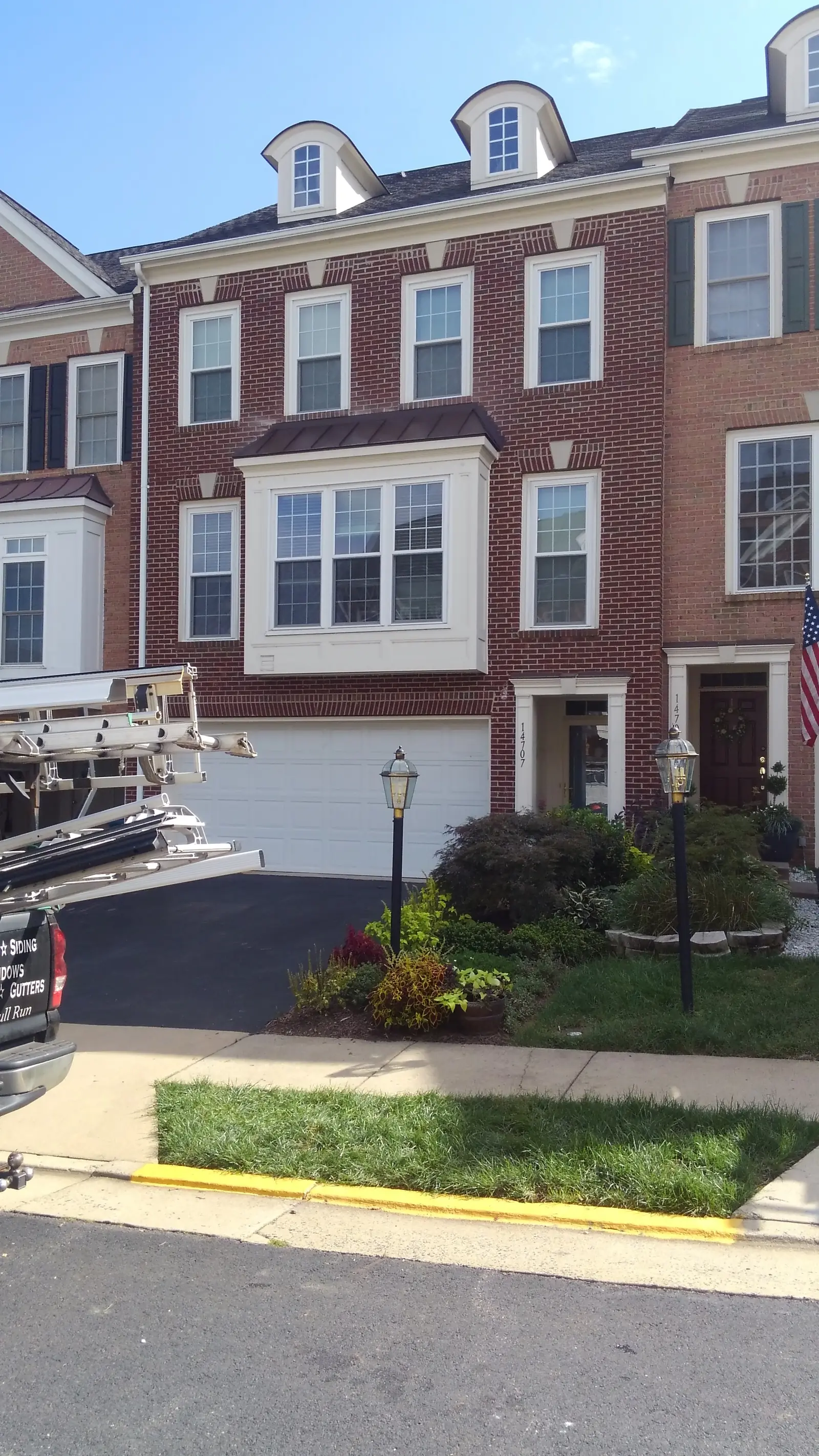Row of brick townhomes with brown metal roofs over bays and entries.