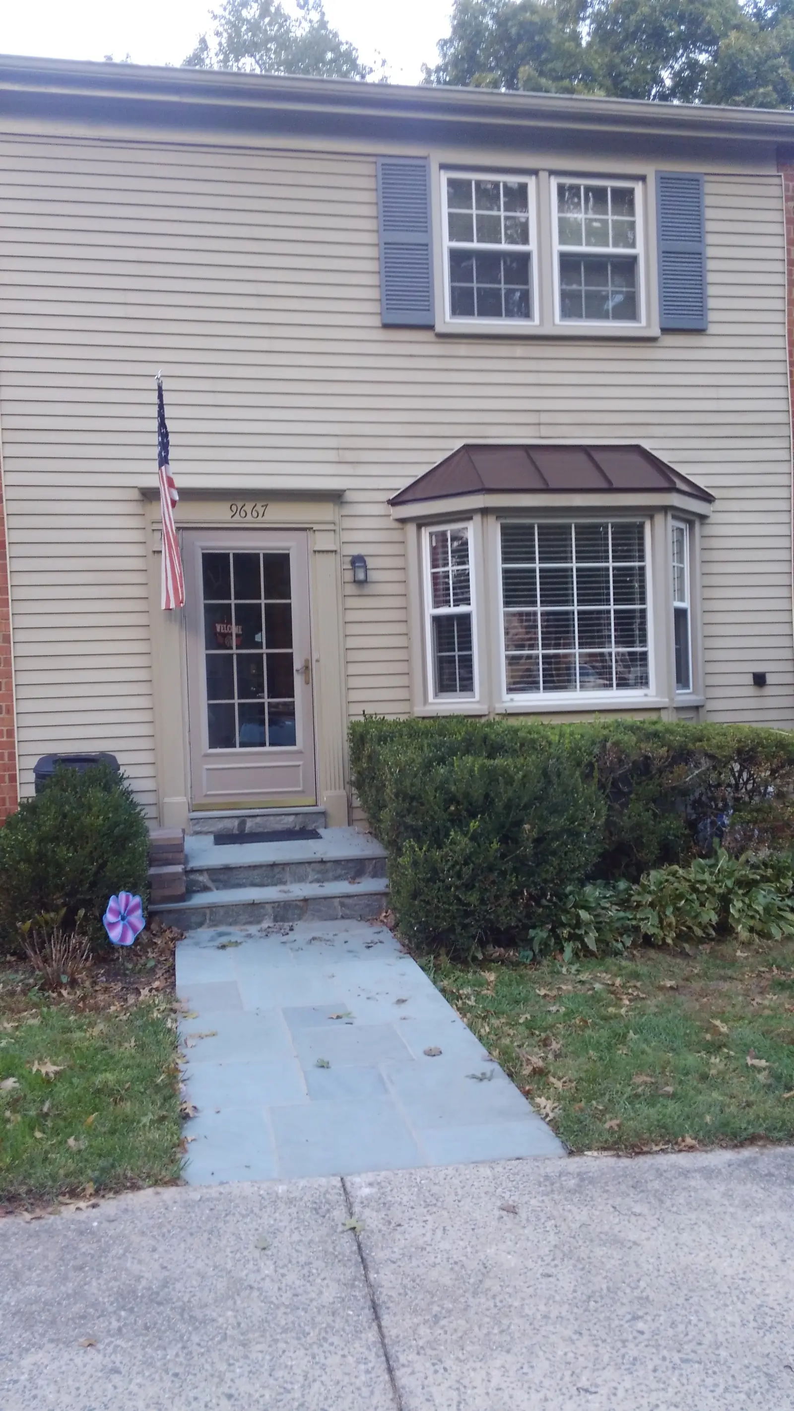 Beige townhome with a bronze metal roof over the front bay and door.