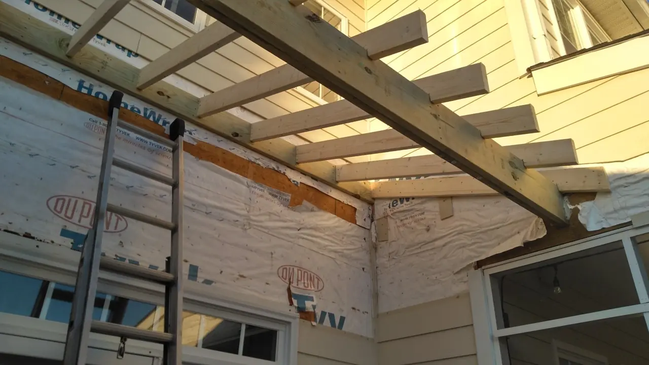 House wrap and a timber beam at a porch corner with a ladder against the wall.