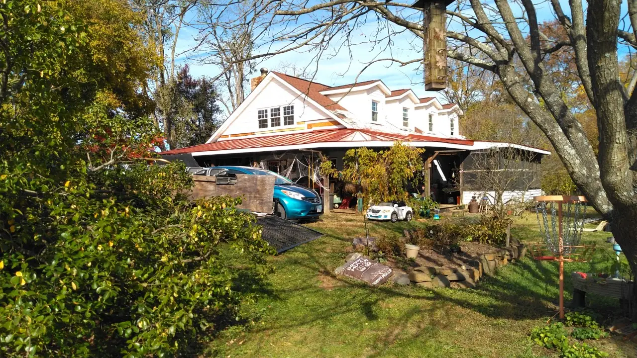 White house with a red standing seam roof, dormers and a porch seen through trees.