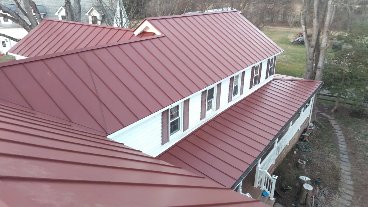 Long red standing seam roof with a row of white dormers above a grassy slope.