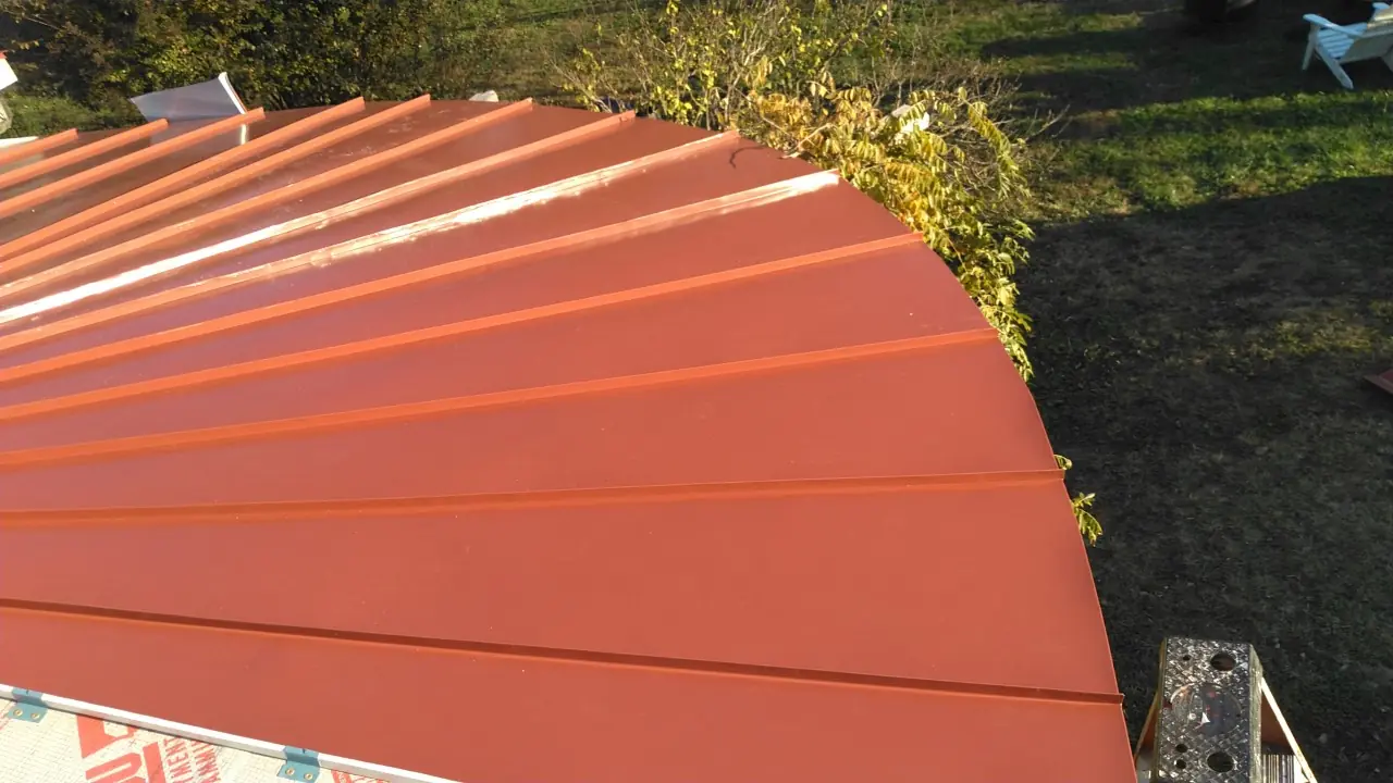 Red standing seam curved roof edge above a lawn.
