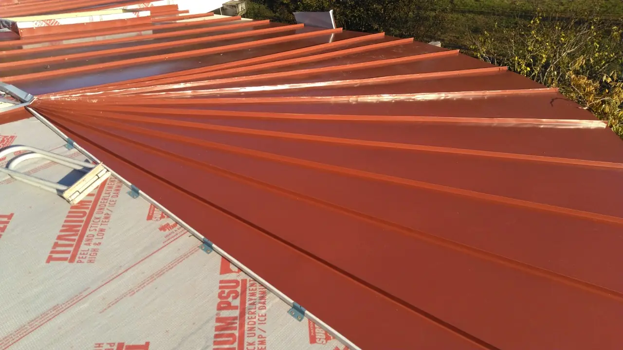 Red standing seam panels meeting underlayment at a roof edge.