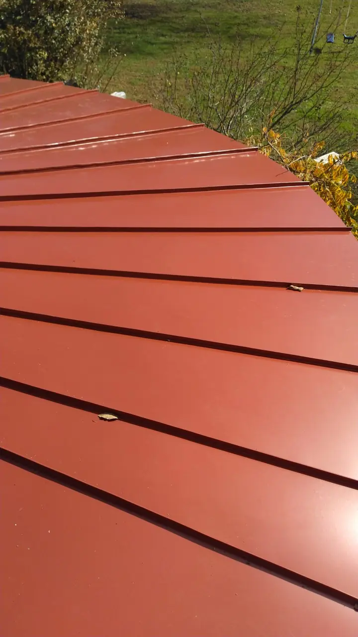 Red standing seam panels turning from straight runs into the curve.