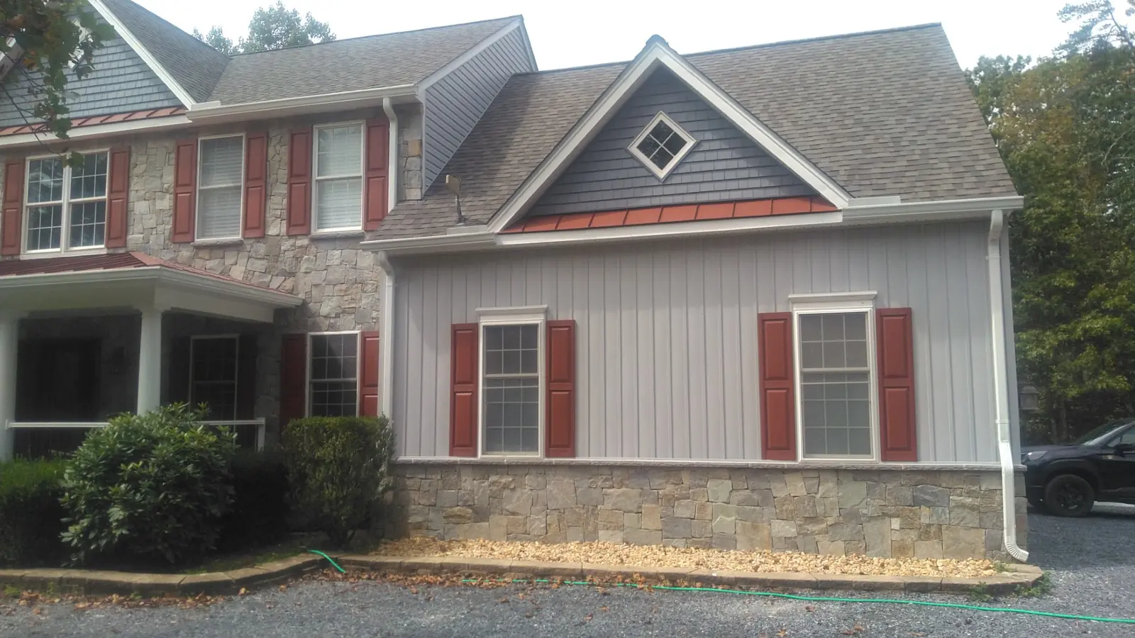 Gable end with dark siding, a red standing seam accent roof, stone and red shutters.