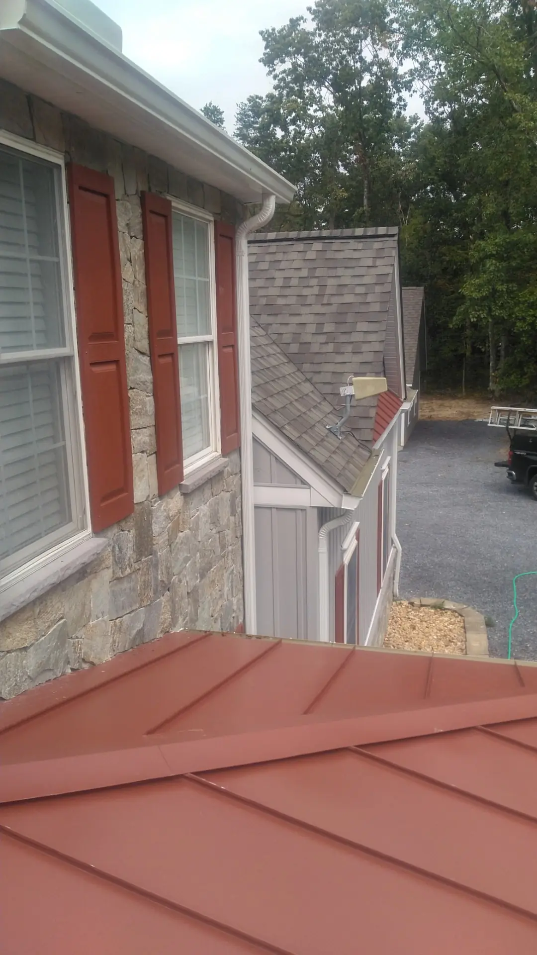 Red standing seam metal roof section beside a stone wall and red shutters.