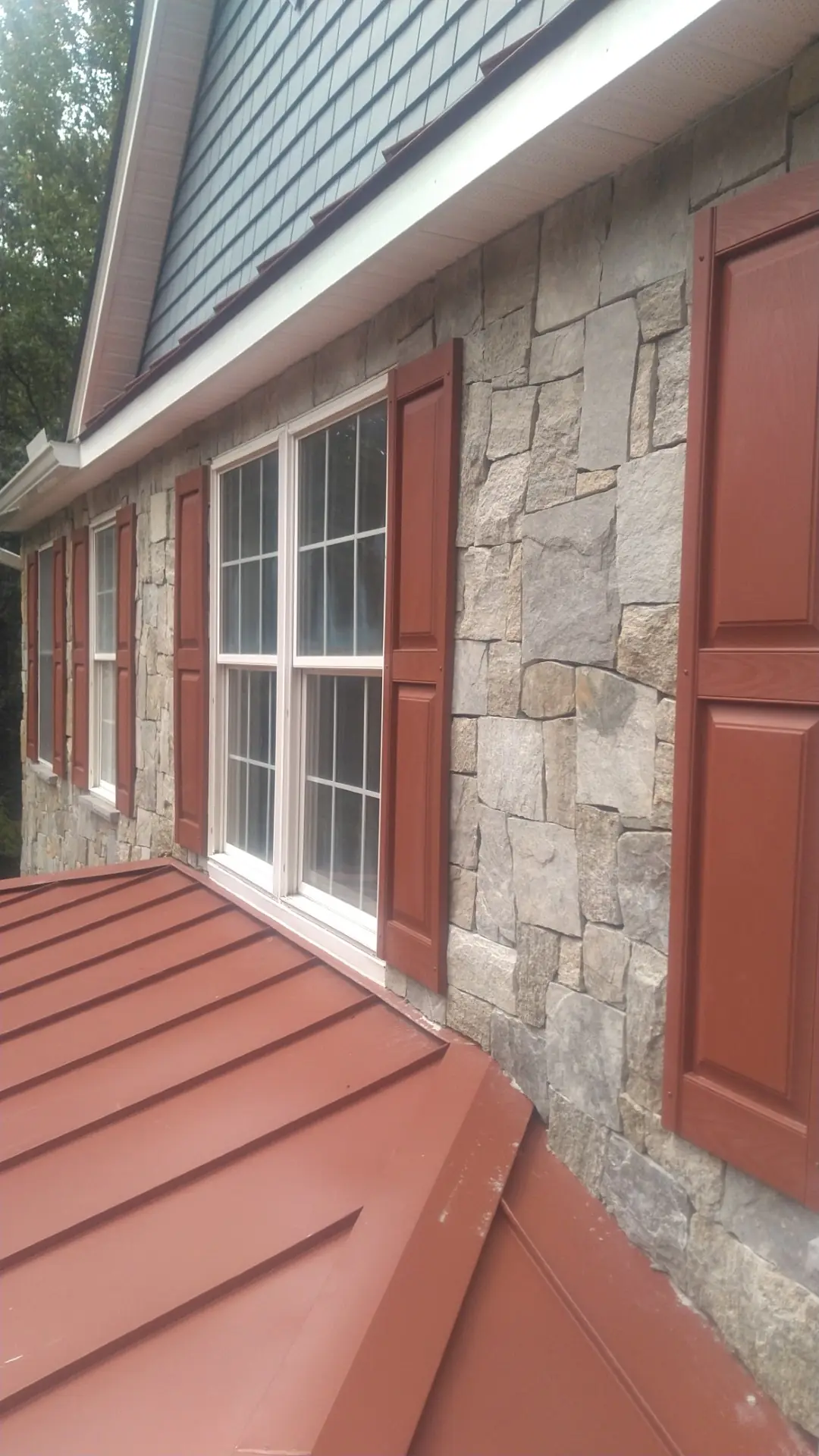 Red metal roof edge meeting a stone wall beside a white window.