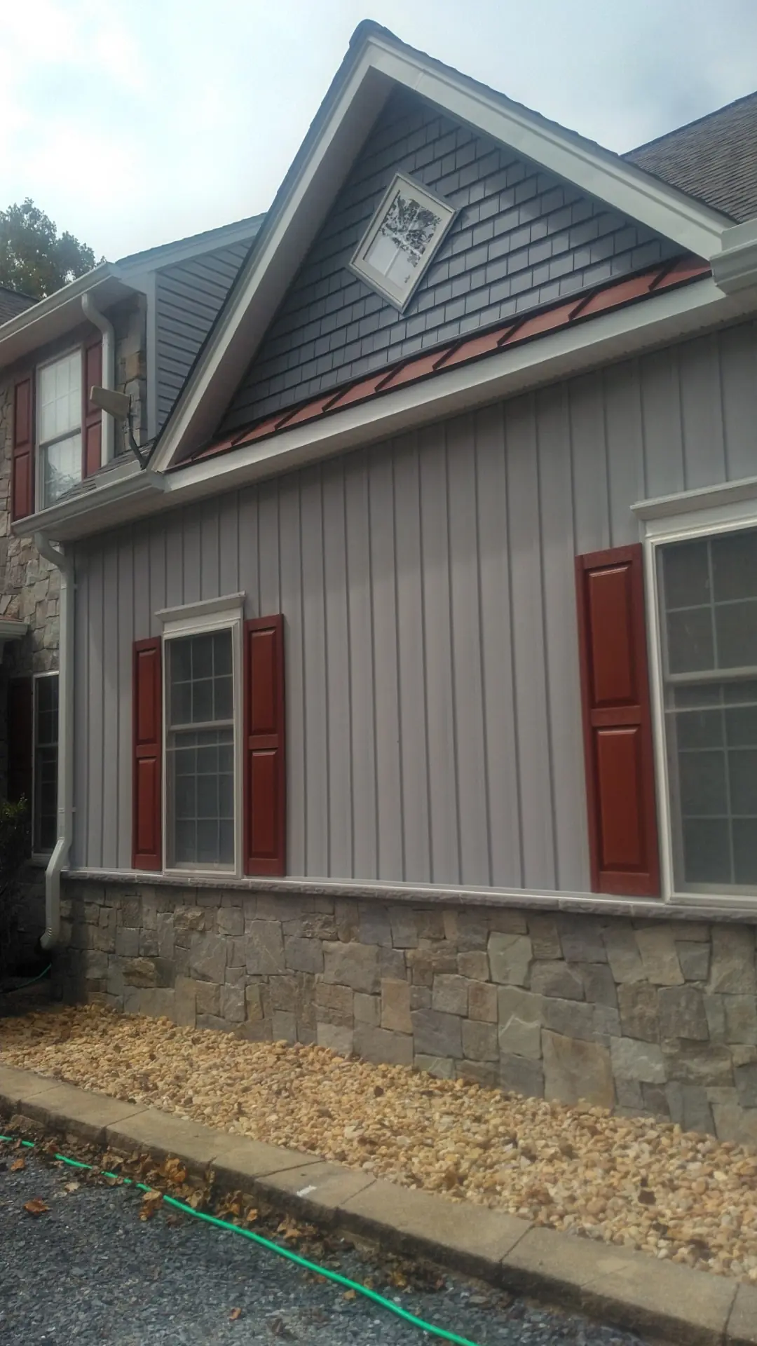Side of the home showing red shutters, stone and the red metal roof above the window.