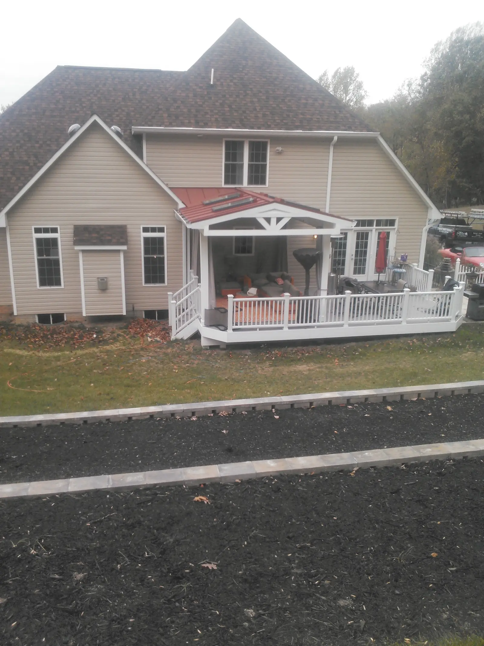 Back of a beige home with a red metal porch roof and white railing.