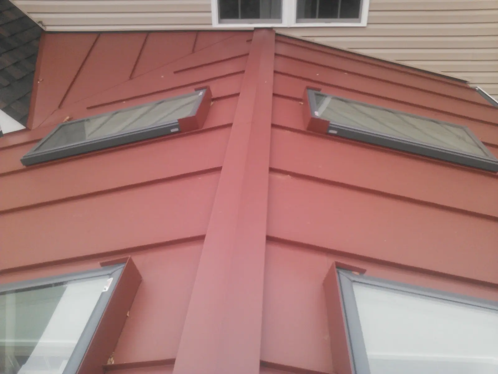 Red standing seam roof with three skylights and a siding wall behind.