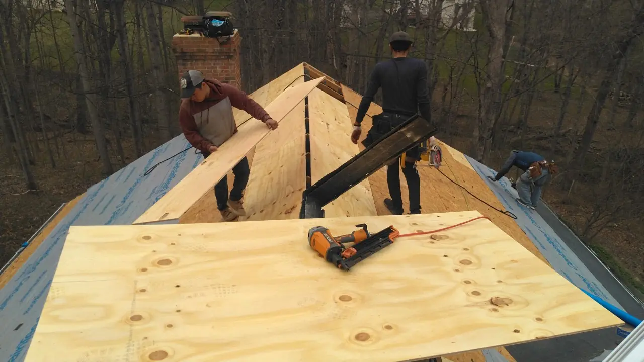 Two crew members fastening new plywood decking beside a brick chimney.