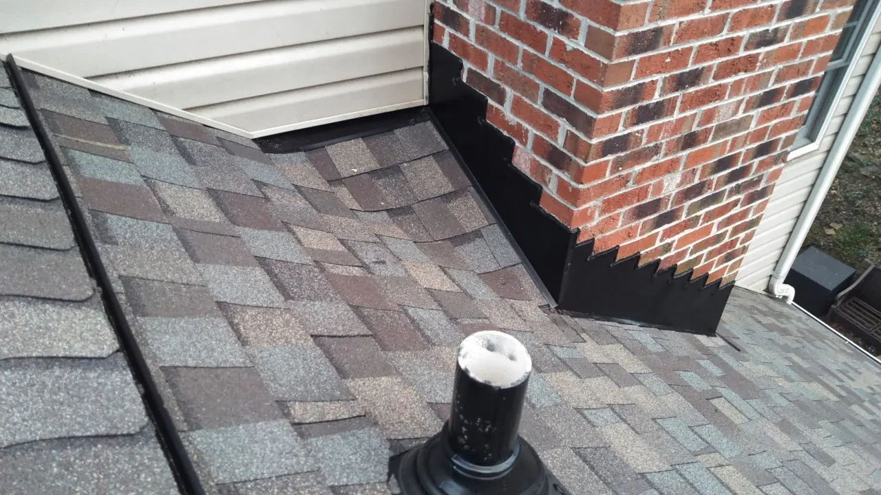 Step flashing at a brick chimney beside new shingles and a vent boot.
