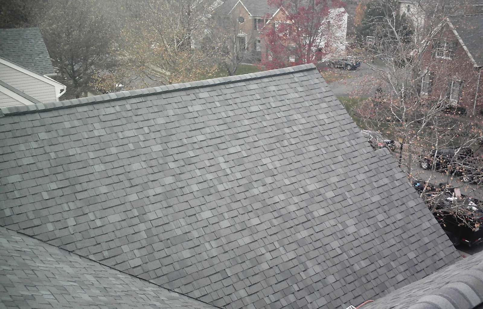 Grey architectural asphalt shingle roof plane with neighborhood trees behind.