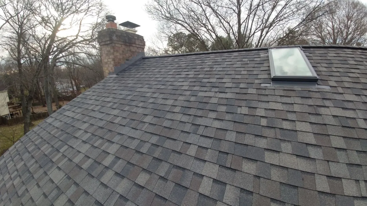Dark asphalt shingle roof with a skylight beside a brick chimney.